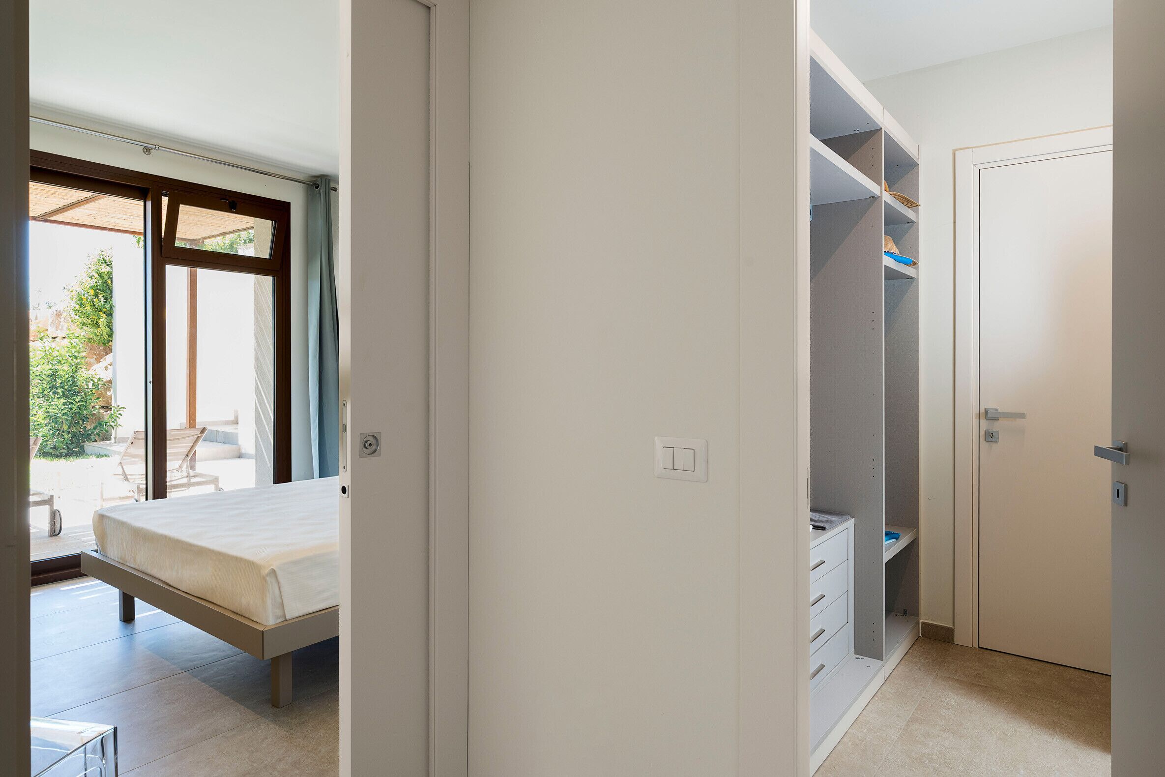 A bedroom with a bed, a closet with shelves, and a sliding glass door to the outside.