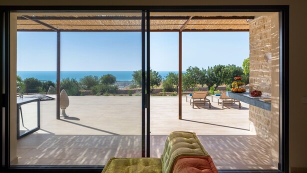 Ein Zimmer mit einer großen SchiebeglasTür, die auf eine Terrasse im Freien mit Blick aufs Meer führt.