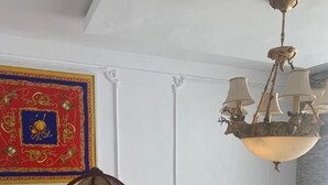 A room with a wooden chair, a red and gold decorative wall piece, a chandelier, and a colorful painting. - TAI HOTEL LEKKI (Lekki)