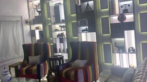A modern living room with a glass coffee table, striped armchairs, a leather sofa, and a wall-mounted shelving unit with decorative items. - TAI HOTEL LEKKI (Lekki)