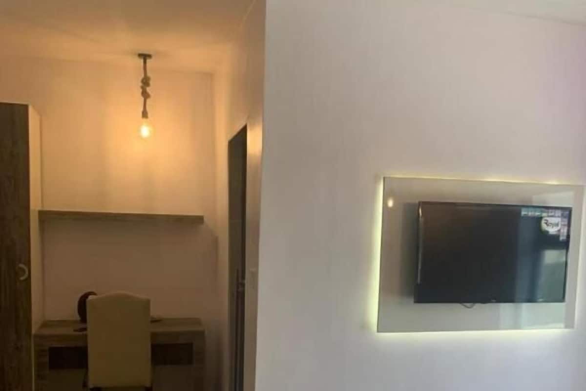 A hotel room with a bed, a desk, a chair, a television mounted on the wall, and a wooden floor.