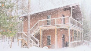Eine zweistöckige Holzhütte mit Balkon, umgeben von Bäumen und bedeckt mit Schnee.