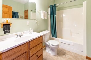 A bathroom with a white sink, wooden vanity, a toilet, a bathtub, and a shower curtain. - Woodland Lodging  |  Apartment near Bayfield (Bayfield)