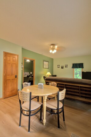 A dining area with a round table, four chairs, a wooden door, and a bench in the background. - Woodland Lodging  |  Apartment near Bayfield (Bayfield)