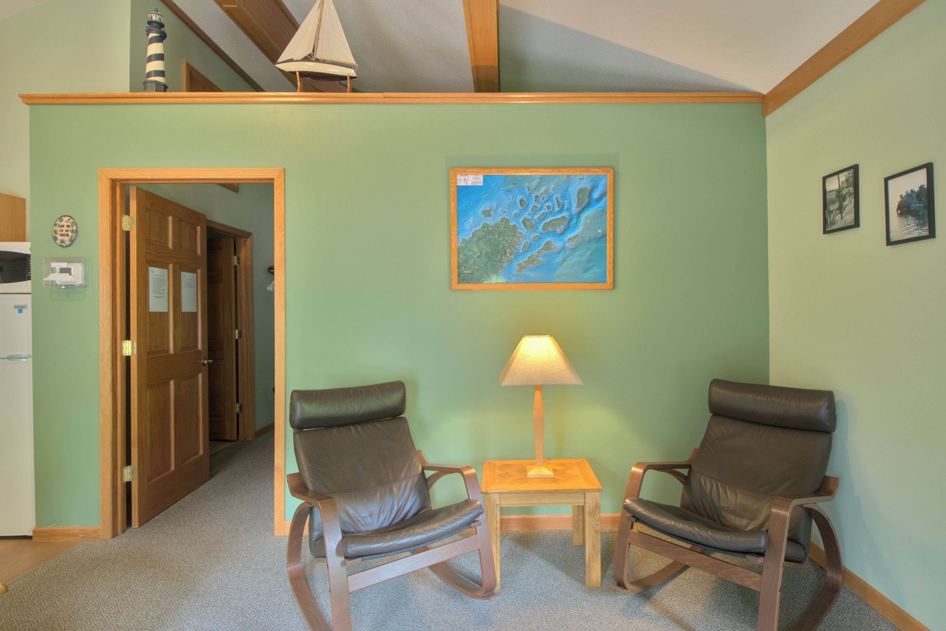 A room with two leather chairs, a small table with a lamp, a framed map on the wall, and a door leading to another room.