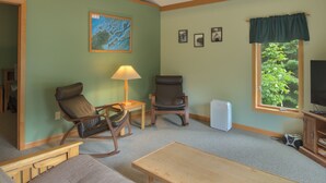 Un salon comprenant un canapé, un fauteuil à bascule, une table, une lampe, un téléviseur et une fenêtre donnant sur des arbres.