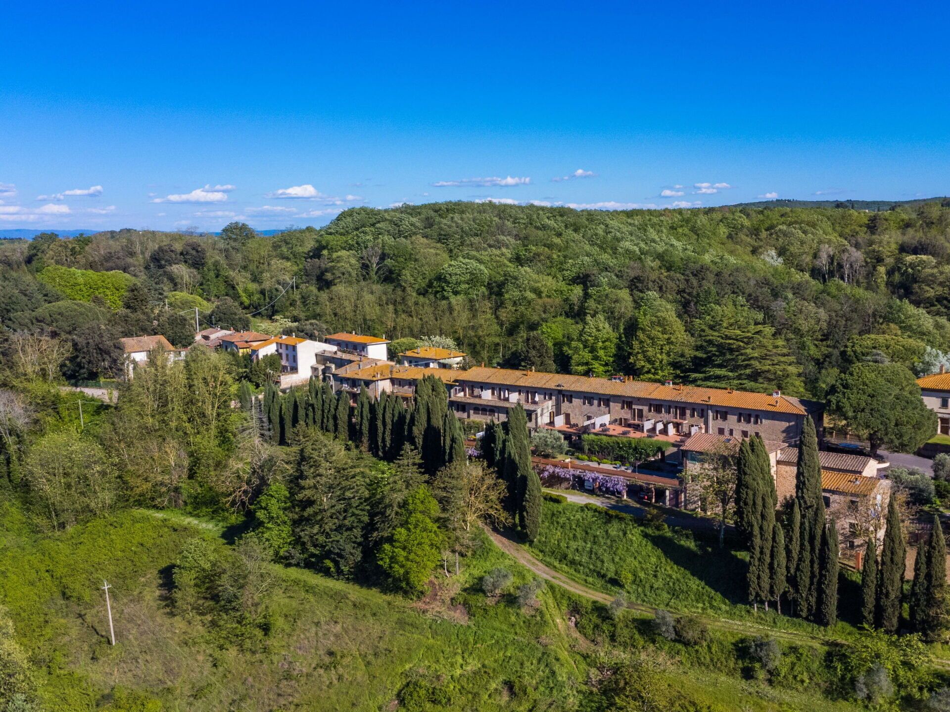 A hillside hotel with terracotta-roofed buildings, surrounded by lush greenery and a clear blue sky.