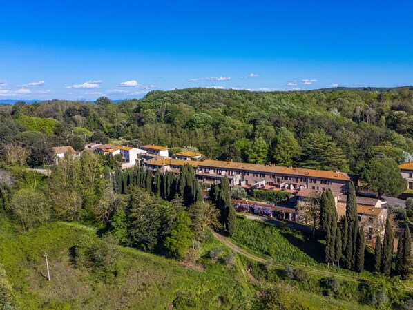 A hillside hotel with terracotta-roofed buildings, surrounded by lush greenery and a clear blue sky.