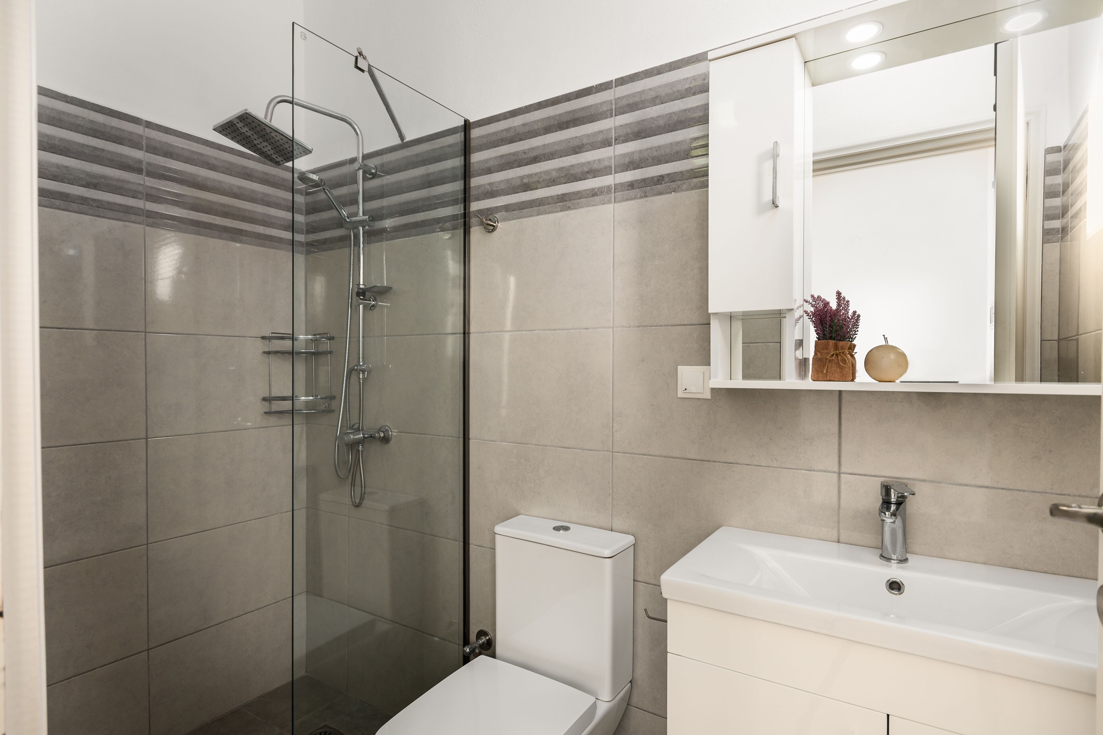 Een moderne badkamer met een douchecabine van glas, een toilet en een wastafel met spiegel erboven.