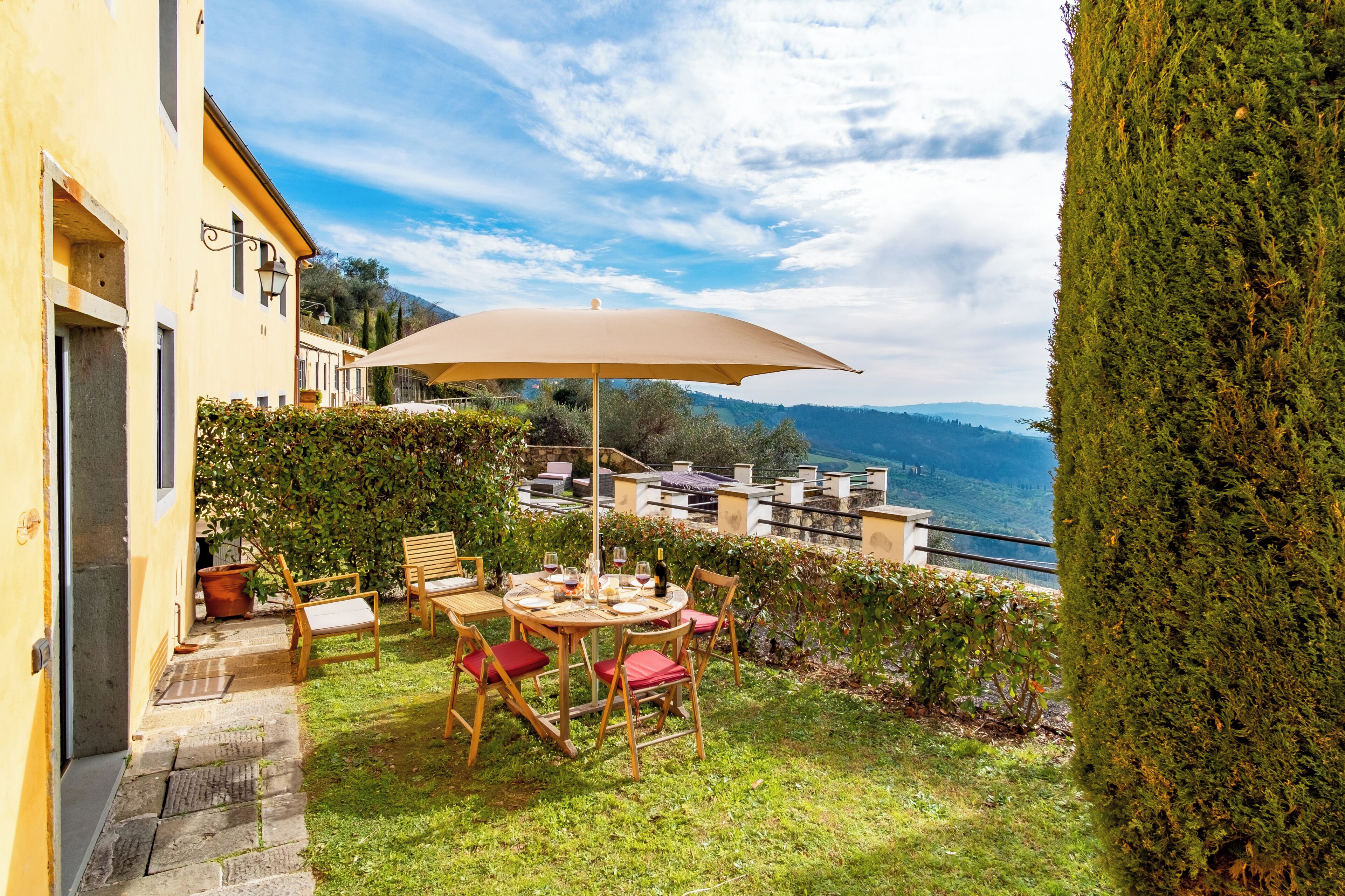 Eine Terrasse mit Tisch und Stühlen, einem großen Sonnenschirm und Blick auf die Berge.