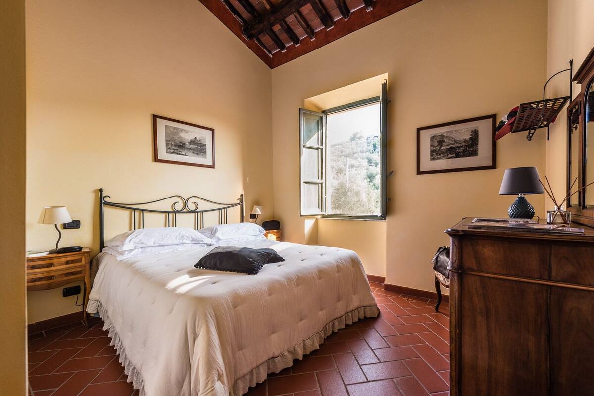 A bedroom with a bed, a nightstand, a dresser, and a window with an open shutter.