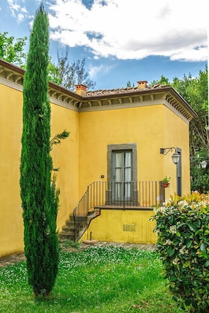 A yellow building with a staircase, a tall green tree, and a small garden. - Tenuta Guinigi Antico Borgo di Matraia   (Capannori)