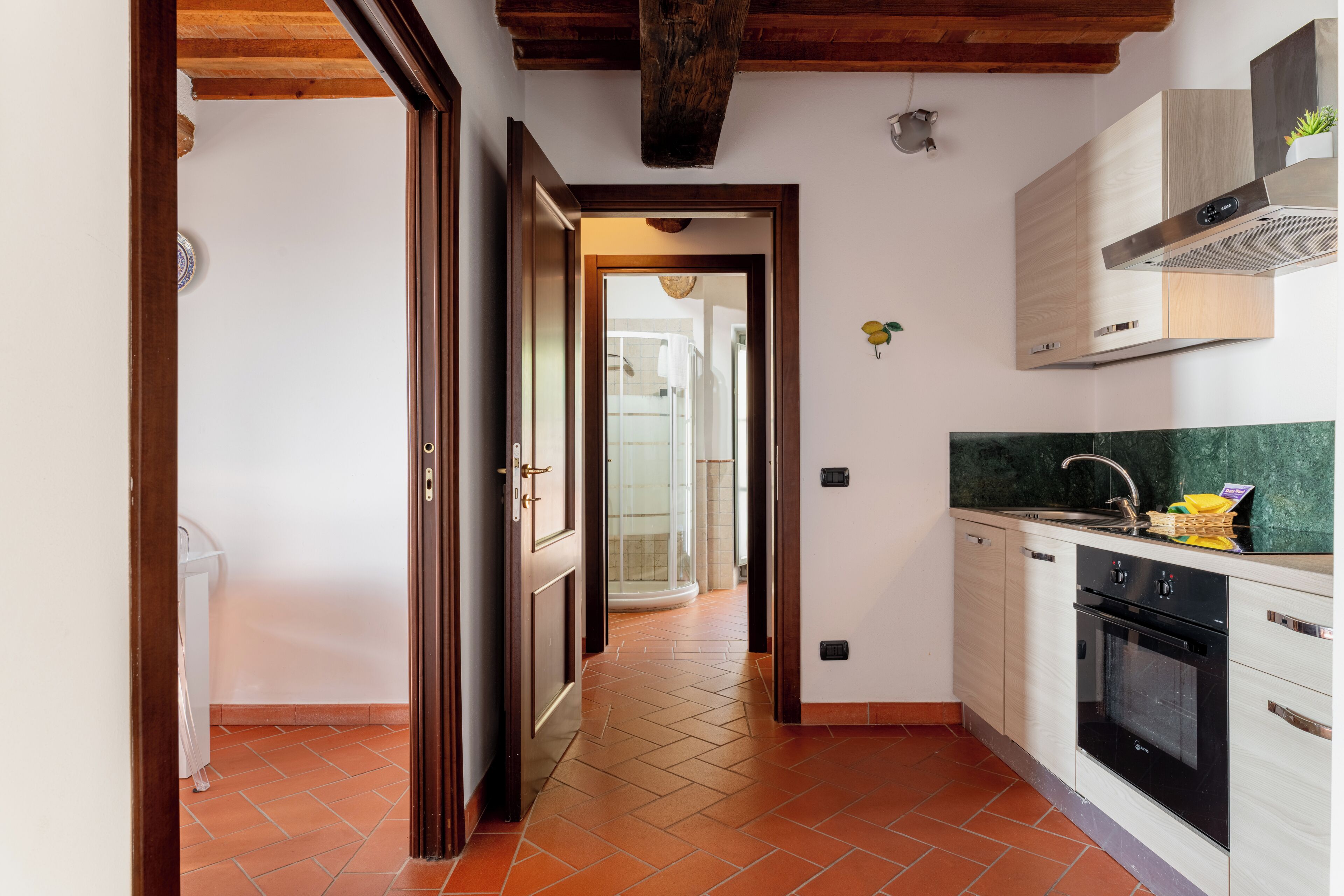 A kitchen with a tiled floor, wooden ceiling beams, a built-in oven, and a stainless steel range hood.