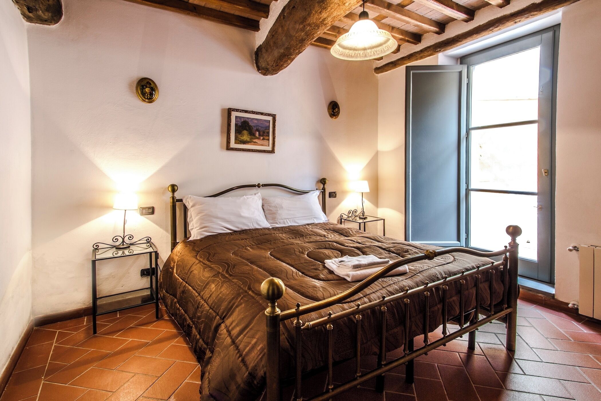 Quarto com cama, duas luminárias de cabeceira, um quadro na parede e uma janela.