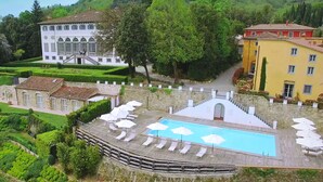 A pool area with lounge chairs and umbrellas, surrounded by a stone wall and lush greenery. - Tenuta Guinigi Antico Borgo di Matraia   (Capannori)