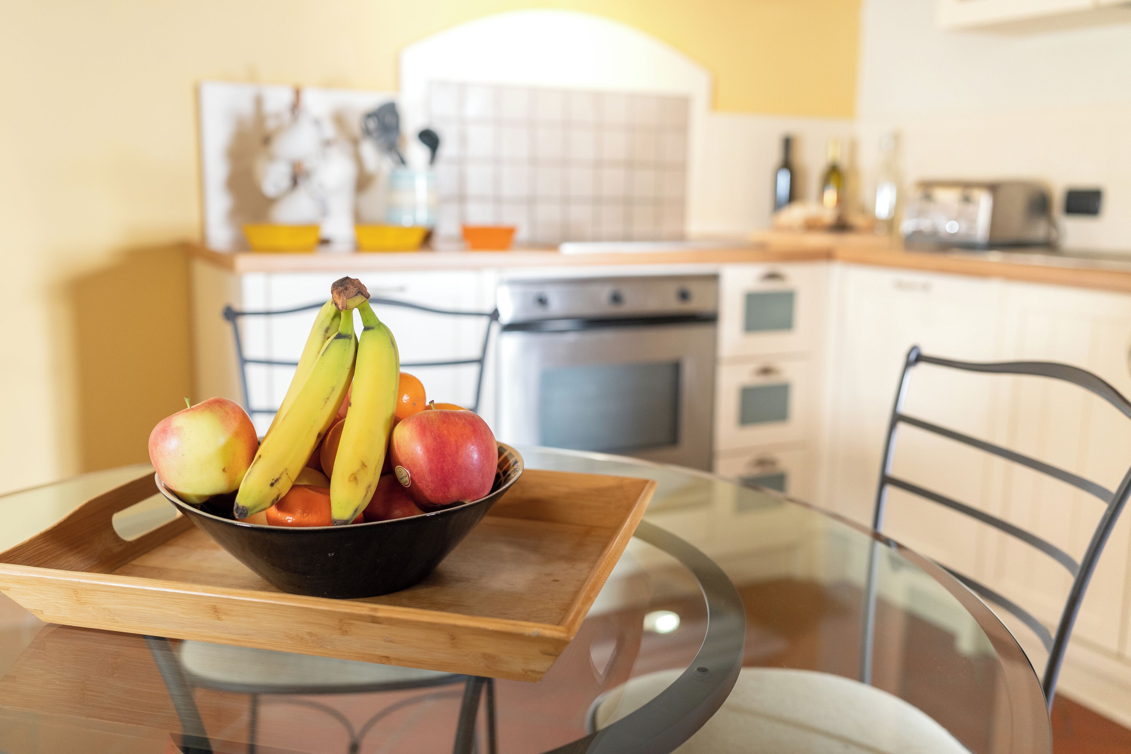 Une table à manger avec un plateau en verre et un plateau en bois sur lequel se trouve un saladier rempli de fruits.