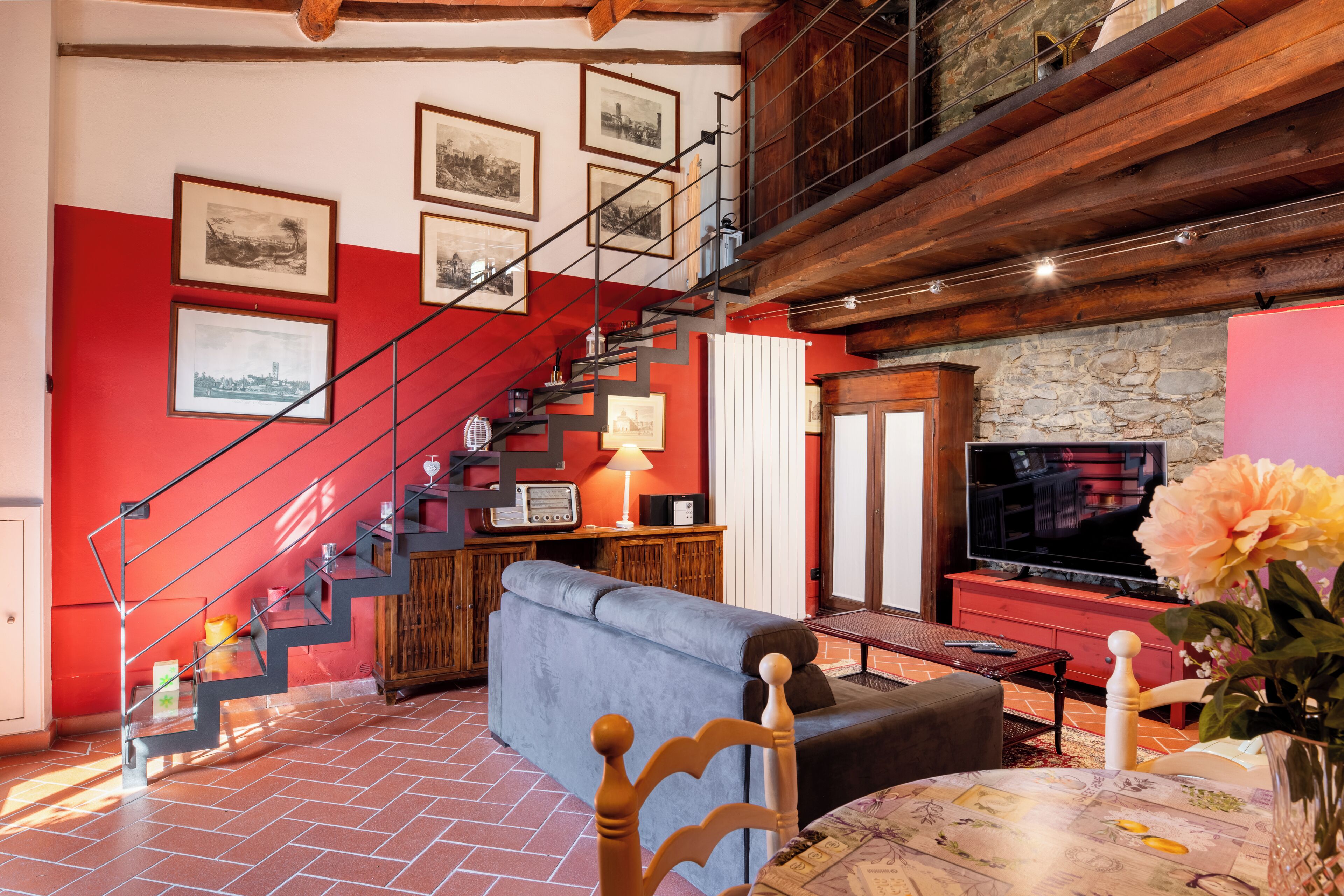 A living room with a red wall, a blue sofa, a wooden staircase, and a television.
