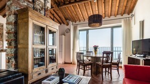 A spacious living area with a wooden ceiling, a stone wall, and a large window overlooking the sea. - Tenuta Guinigi Antico Borgo di Matraia   (Capannori)