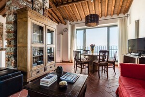 Un amplio salón con techo de madera, pared de piedra y un gran ventanal con vistas al mar.