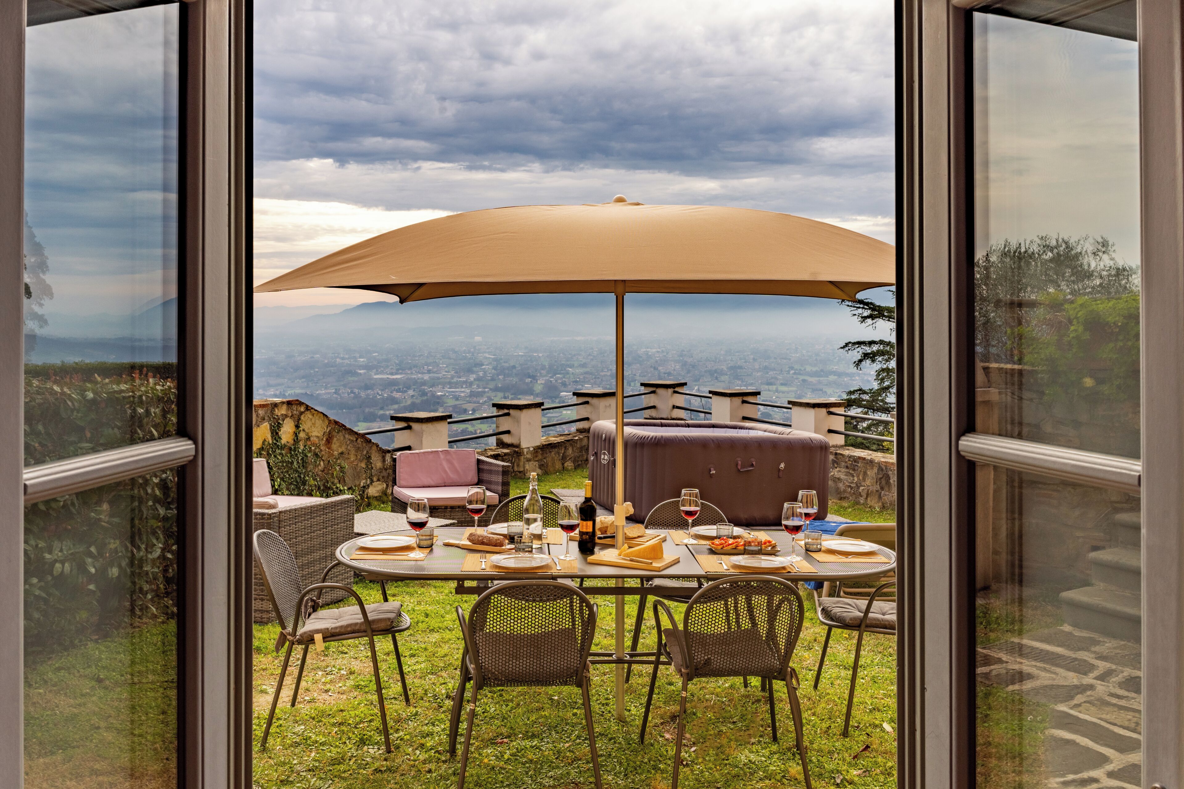 Uma área de refeições ao ar livre com uma mesa posta para quatro pessoas, um grande guarda-sol e uma vista panorâmica da cidade e das montanhas.