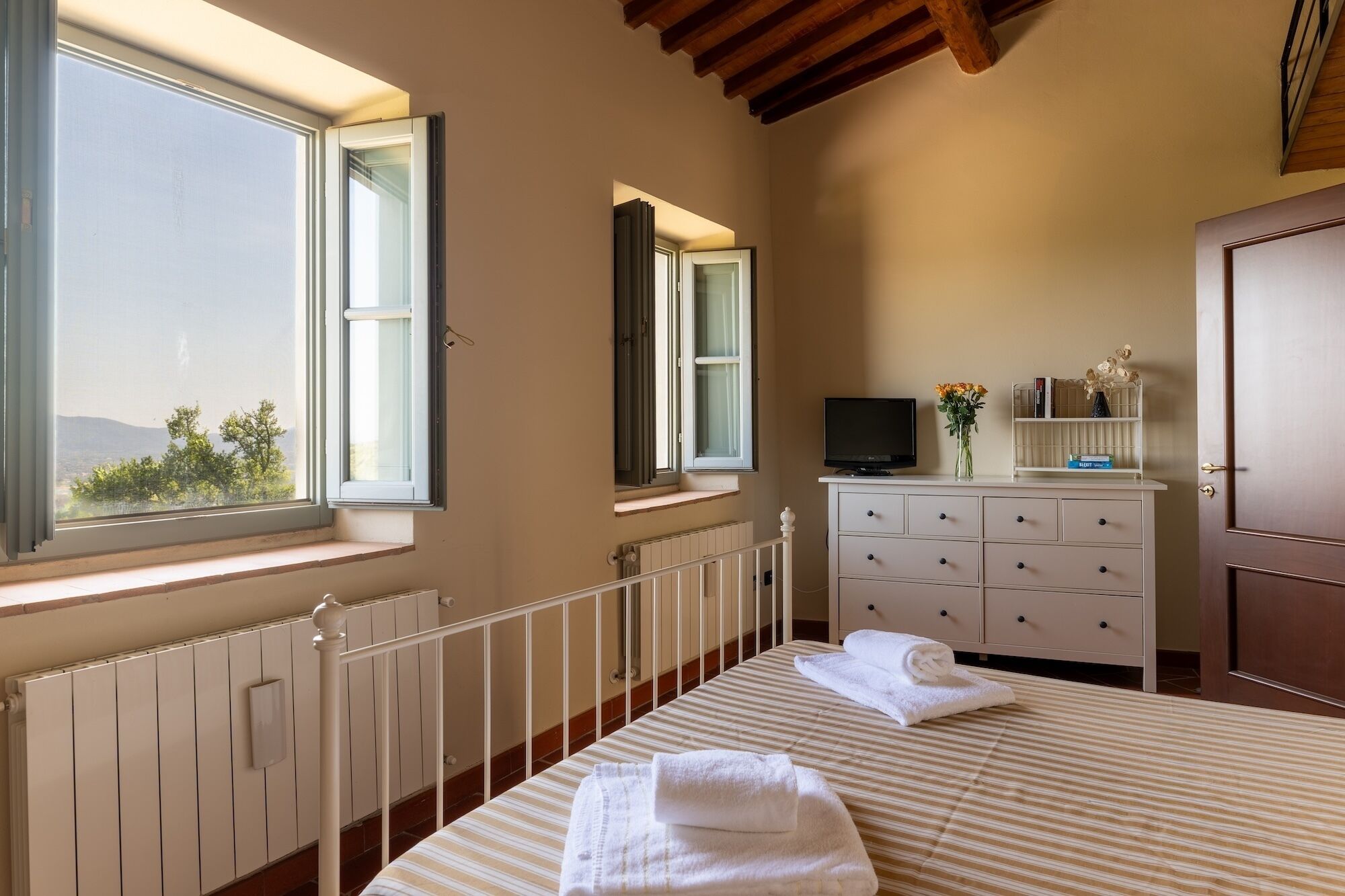 A bedroom with a bed, a dresser, a TV, and a window with a view.