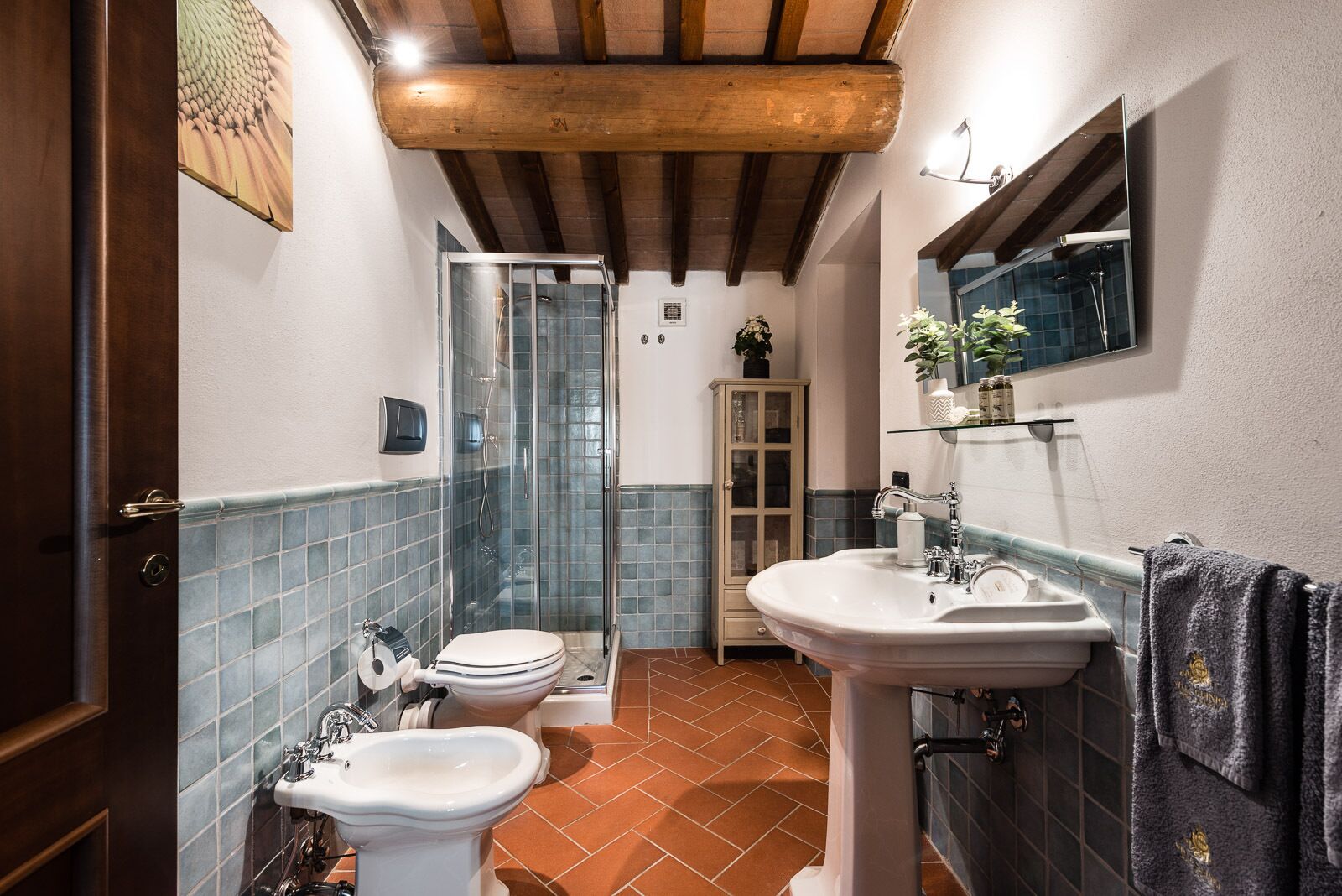 Un baño con cabina de ducha de vidrio, inodoro blanco, bidé y lavamanos con espejo superior.