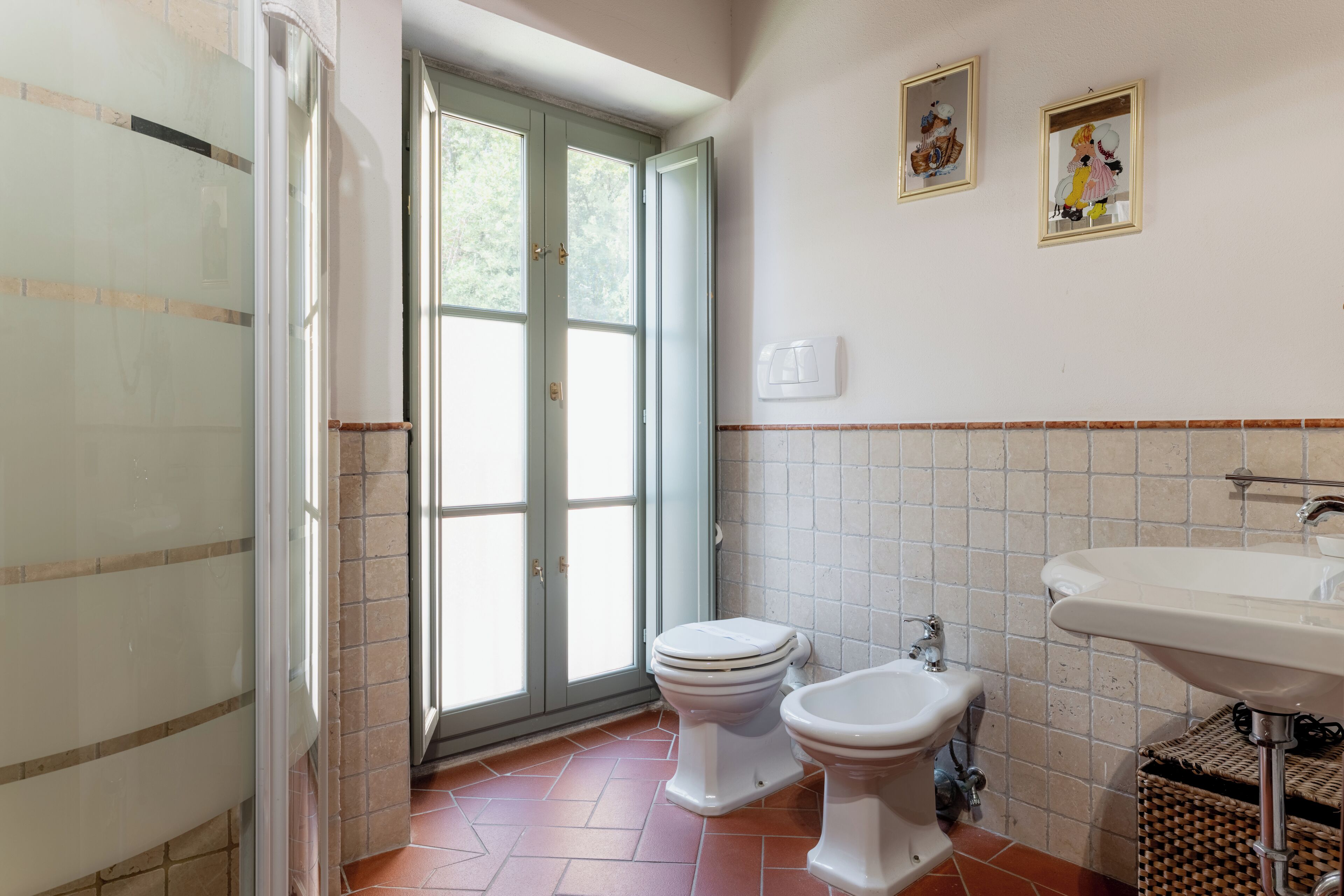 Un baño con inodoro, bidé y lavamanos, suelo de baldosas y una puerta que da a un balcón.