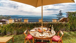A round wooden table with chairs, a table umbrella, and a bottle of wine. - Tenuta Guinigi Antico Borgo di Matraia   (Capannori)