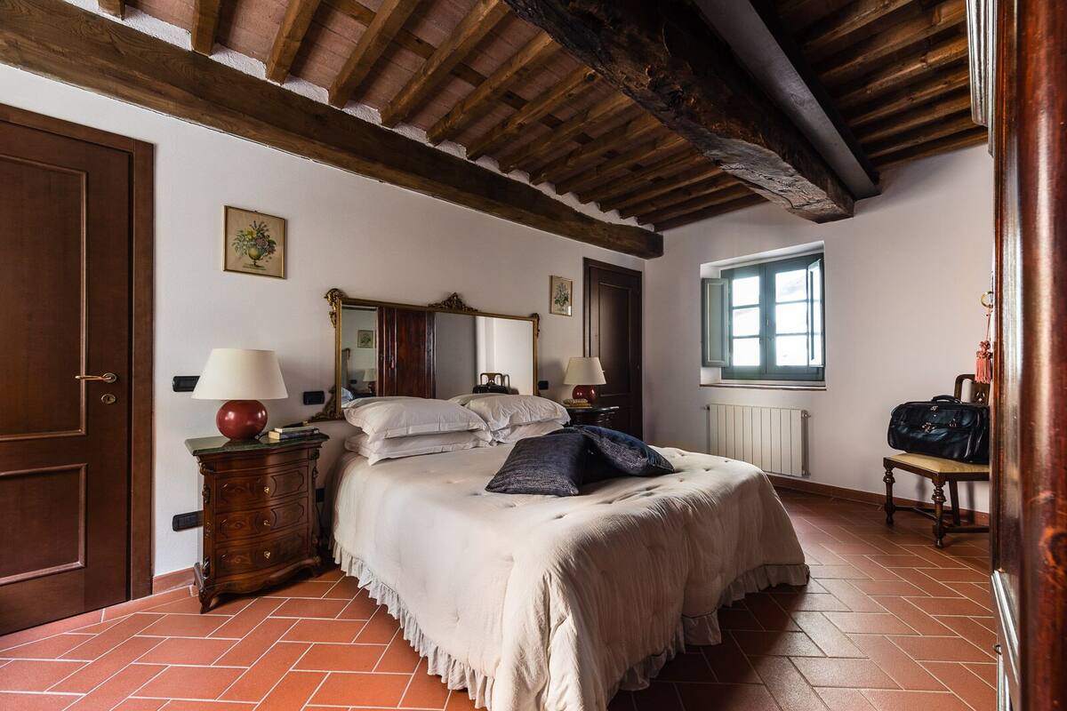 A bedroom with a bed, wooden headboard, a dresser, a mirror, a window, and a suitcase.