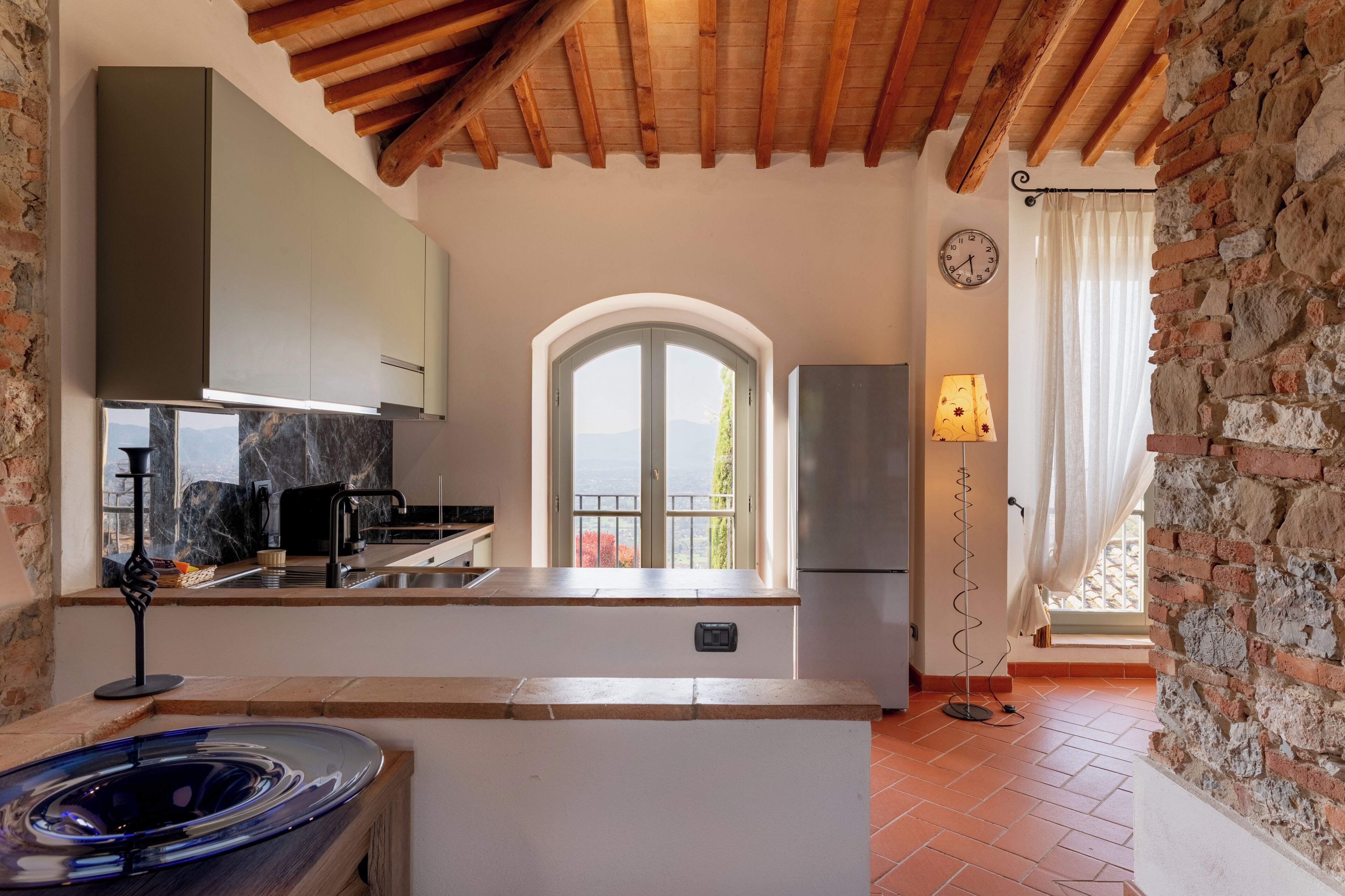 Uma cozinha com bancada de mármore, forno embutido, geladeira e janela com vista.