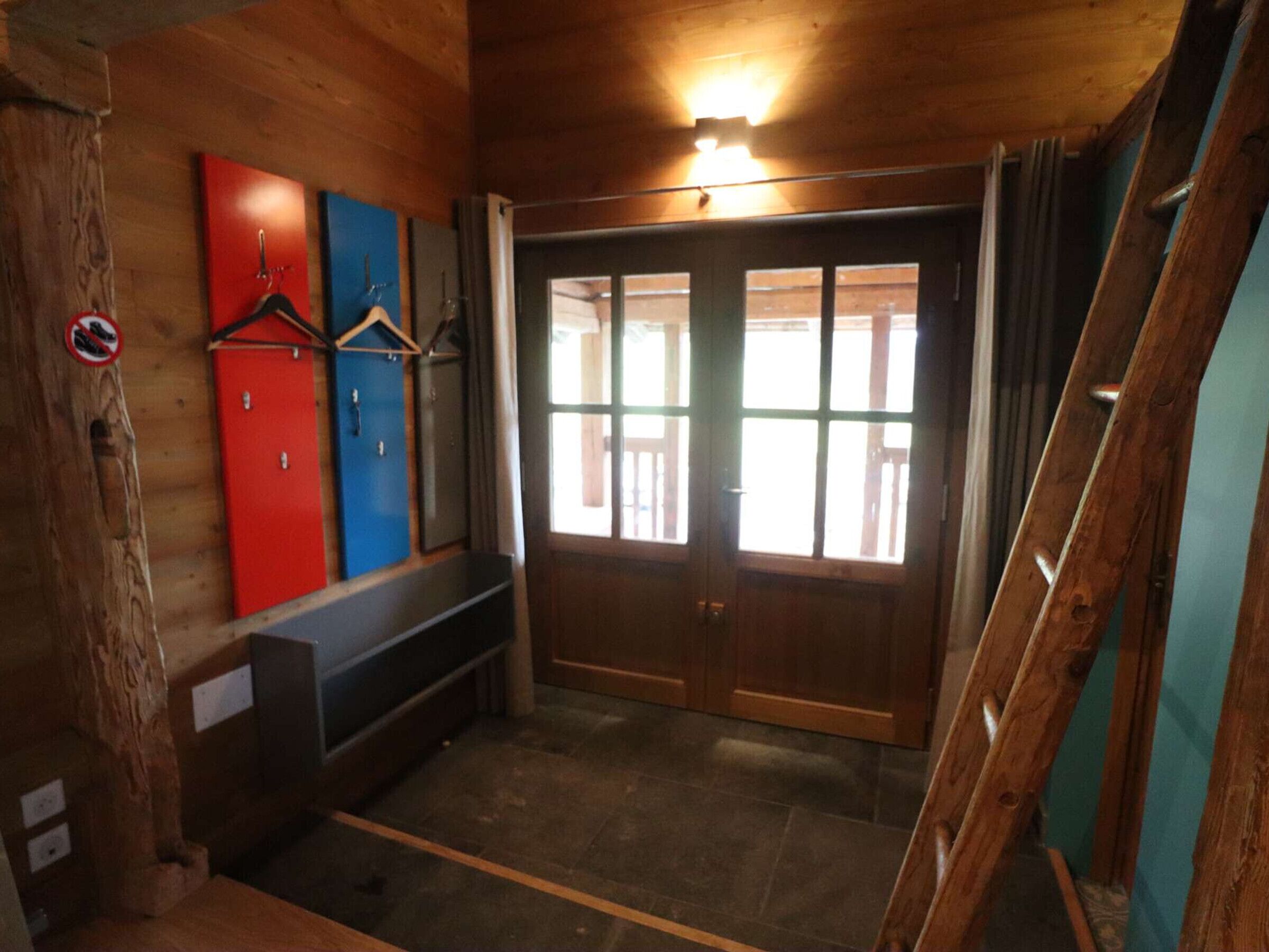 Un interior de madera con un banco, una puerta con paneles de vidrio y un perchero en la pared.