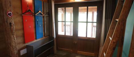 Un interior de madera con un banco, una puerta con paneles de vidrio y un perchero en la pared.