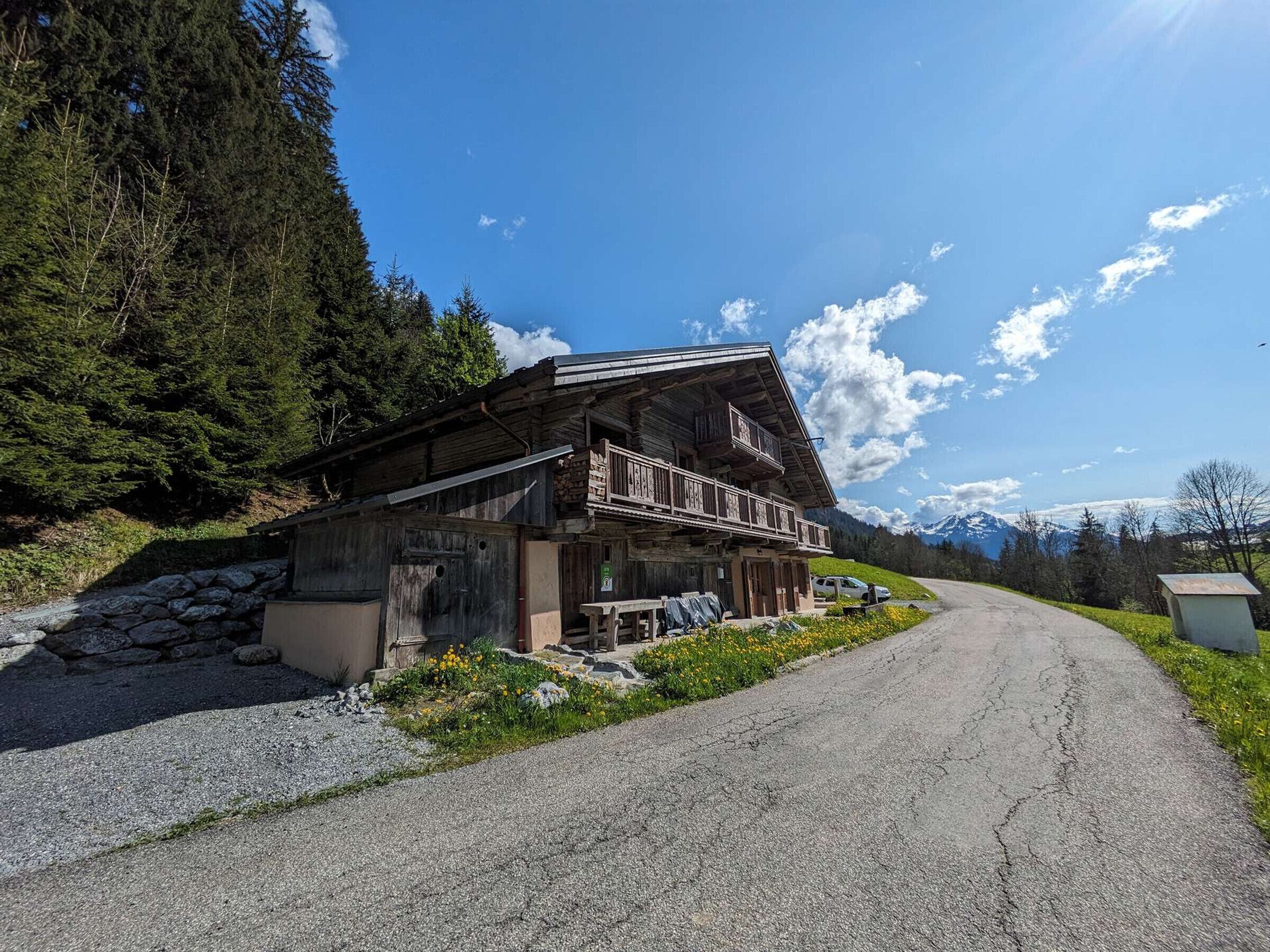 Ein rustikales Holzhaus mit Balkon, einer Schotterzufahrt und einer Bergliege.