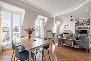 A spacious living room with a wooden dining table, a grey sofa, and a bookshelf. - Bright Skies, by Veeve (Paris)