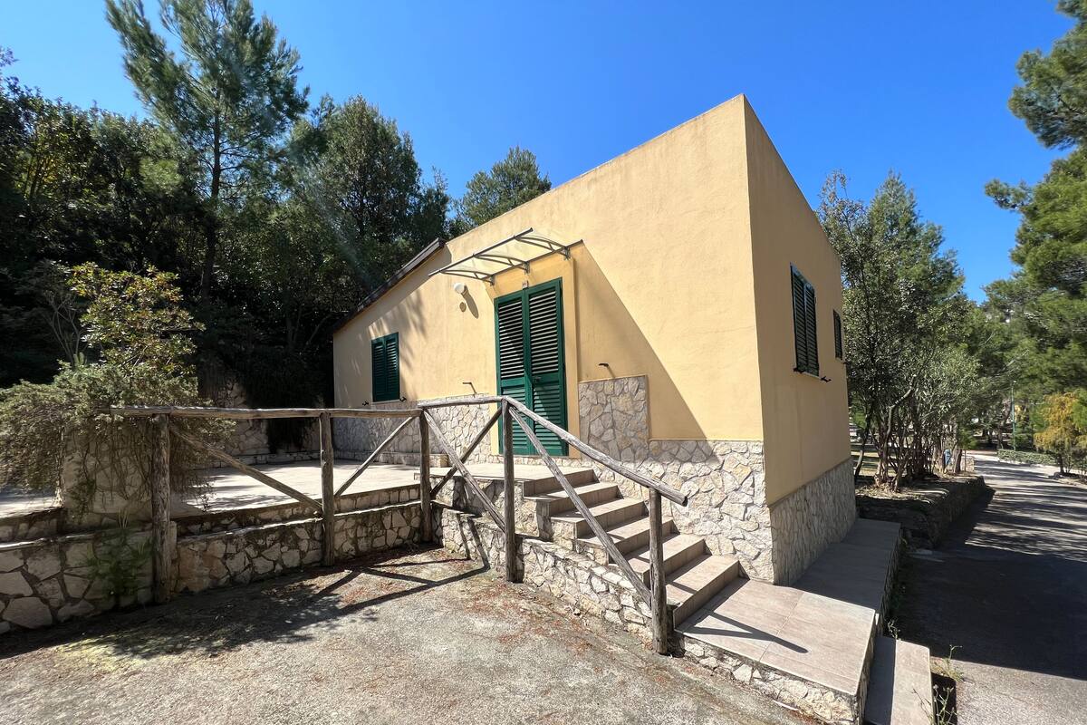 A small building with a stone staircase leading to a door with green shutters.