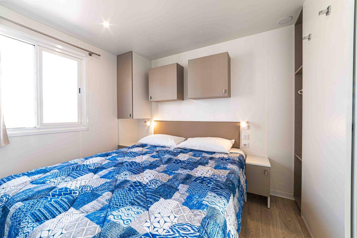 A bedroom with a large bed, a nightstand, a wardrobe, and a window.