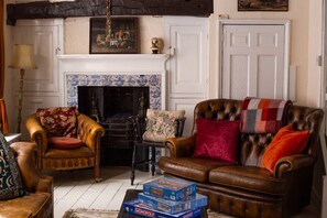 A traditional living room with a fireplace, leather armchairs, a sofa, and a game table with Monopoly boxes.