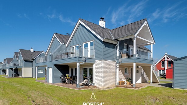 A modern residential building with a two-story design, featuring balconies, a covered patio, and a brick foundation. - Stilvolle Ferienwohnung mit Sauna, Kamin, Terrasse und Wassernähe (Büsum)