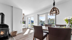 A modern kitchen with a built-in wood stove, a dining area with a table and chairs, and a large window offering a view of the outdoors. - Stilvolle Ferienwohnung mit Sauna, Kamin, Terrasse und Wassernähe (Büsum)