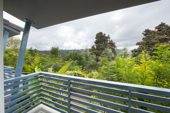 Un balcon donnant sur un jardin luxuriant et sur des collines lointaines.