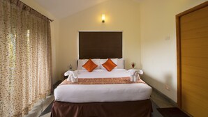 A hotel room with a large bed, two pillows, a headboard, a wall-mounted light, and a wooden door. - TGI Kairos (Tirupattur)