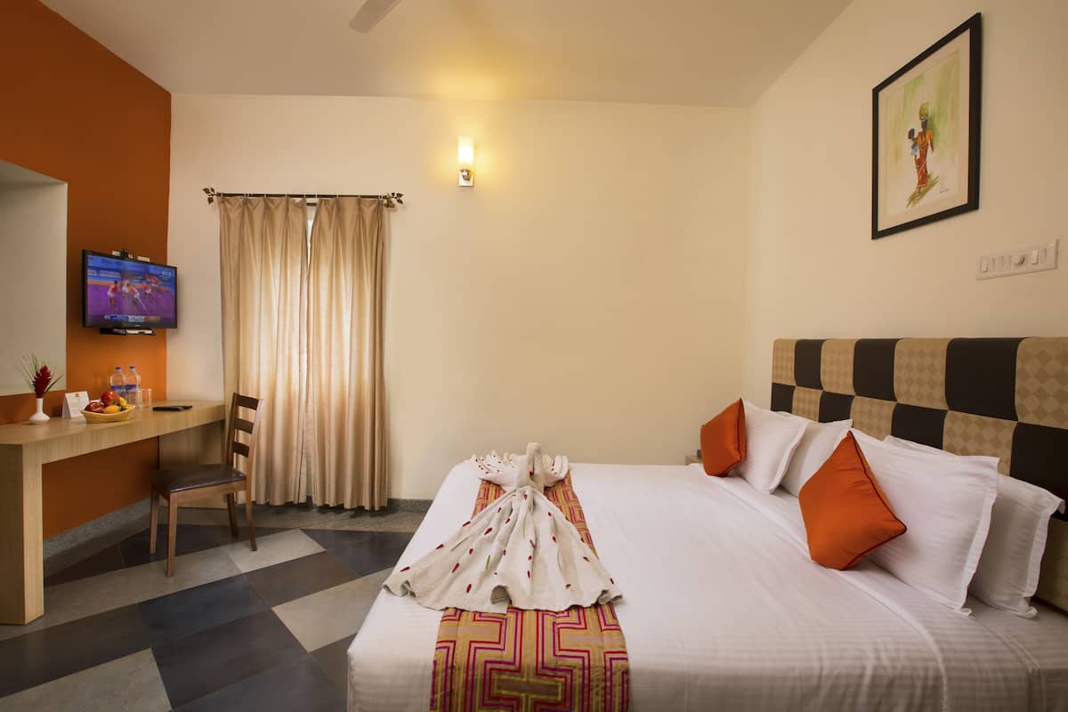 Habitación de hotel con cama, escritorio, televisor y ventana con cortinas.
