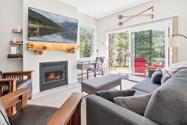 A modern living room with a fireplace, a large window, and a view of a lake and mountains.