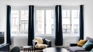 Ein modernes Wohnzimmer mit einer Couch, einem Sessel, einem kleinen Tisch und Blick durch große, mit Vorhängen drapierten Fenster.