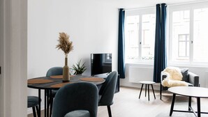 Ein modernes Wohnzimmer mit Essbereich, einer Couch, einem Fernseher und einem Fenster mit Vorhängen.