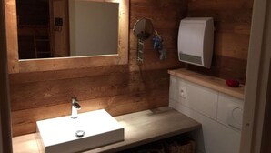 A bathroom with a wooden wall, a large mirror, a white sink, and a towel rack. - Spacious 3-Room Apartment for 6 with Balcony in Châtel, Near Chairlift (Châtel)