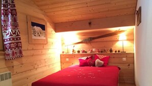 A cozy wooden cabin bedroom with a red bedspread, a small dresser with decorative items, and a wall-mounted shelf. - Spacious 3-Room Apartment for 6 with Balcony in Châtel, Near Chairlift (Châtel)