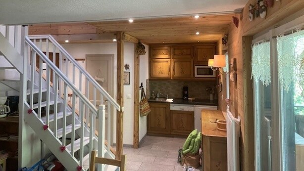 A kitchen with wooden cabinets, a microwave, and a sink. There is a staircase with white railings leading to another room. - Spacious 3-Room Apartment for 6 with Balcony in Châtel, Near Chairlift (Châtel)