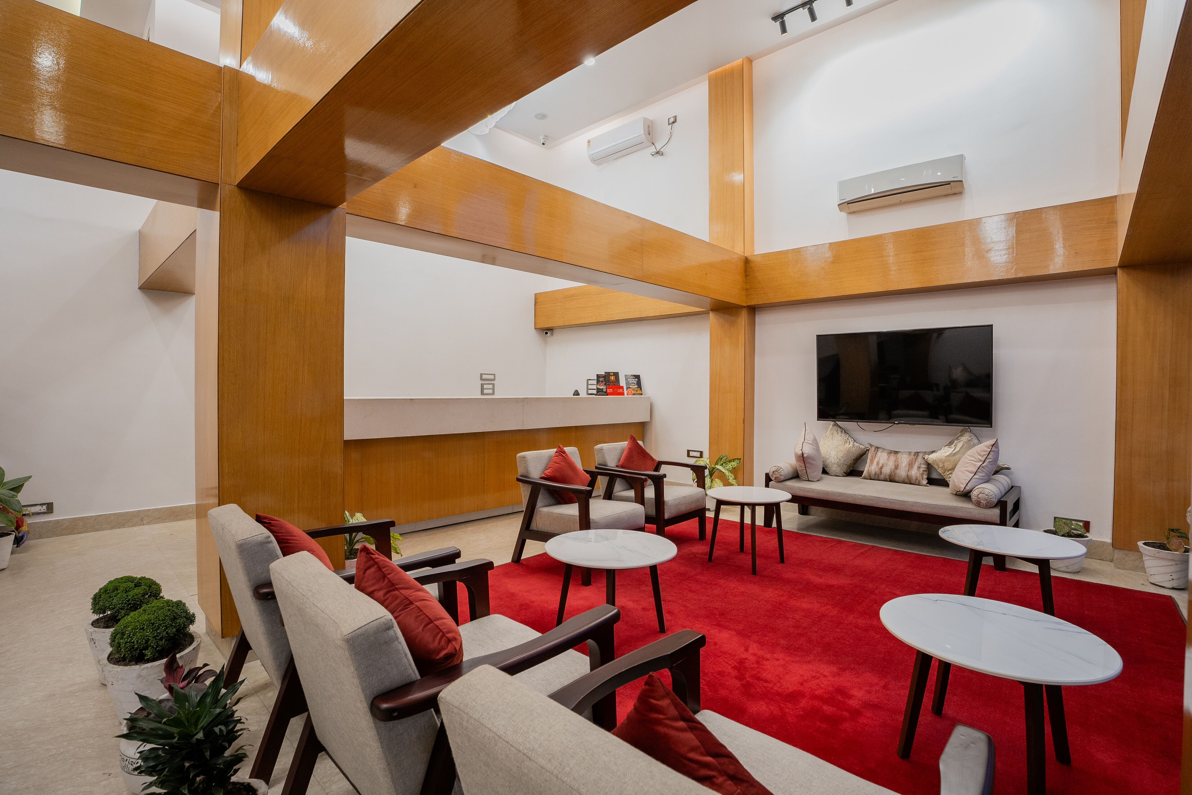 Un moderno espacio de descanso con sofás, sillones y mesitas, destacando una alfombra roja y detalles de madera.