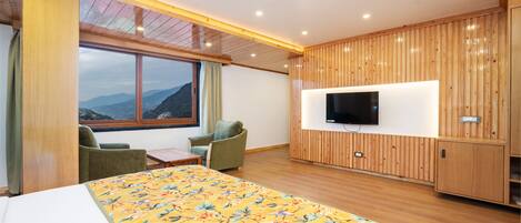 Una camera d'albergo con un letto, due poltrone, una televisione e un'ampia finestra vista montagna.